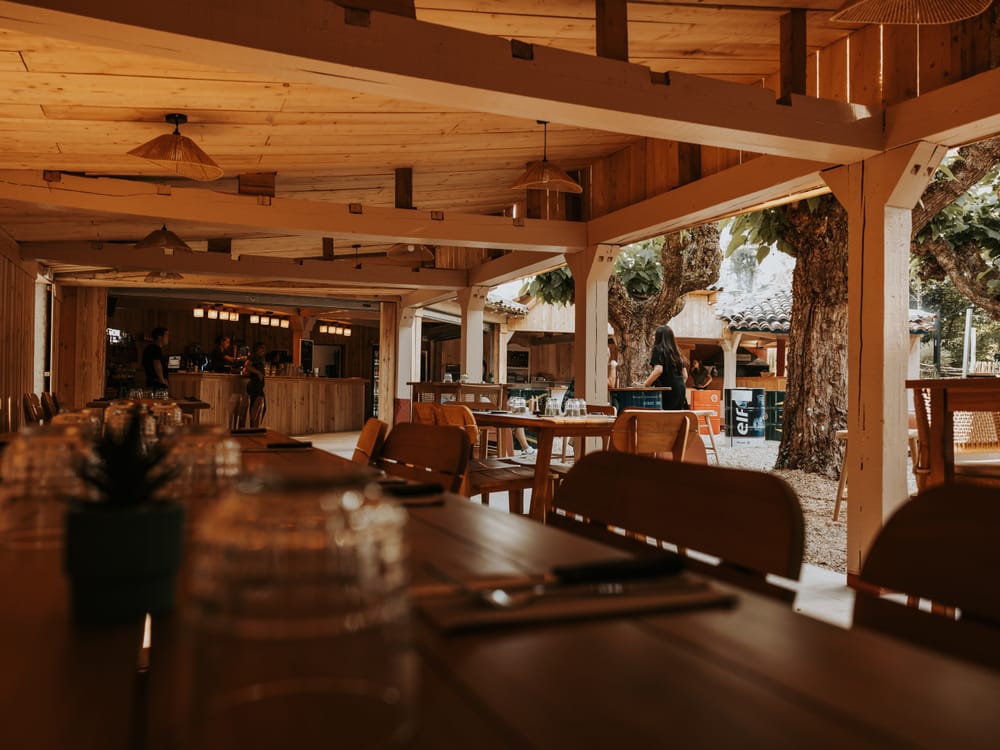 L'intérieur de L'Espagnette : le bar en bois et les tables dressées sous la charpente, ouvert sur la terrasse à Moissac