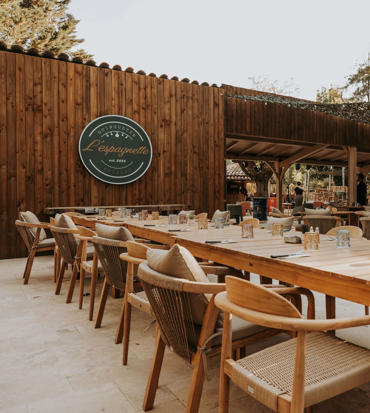 La terrasse de L'Espagnette avec l'enseigne de la guinguette au mur, longues tables et fauteuils en bois, au bord du canal à Moissac